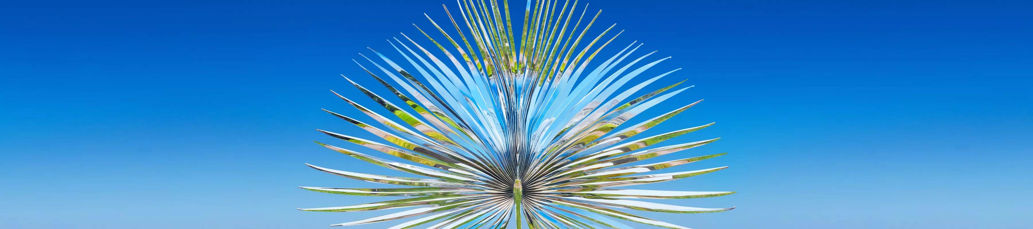 Reflective metal sculpture of palm frond against a blue sky