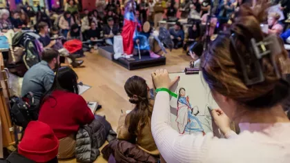 A large crowd of people drawing a person in the centre of a room