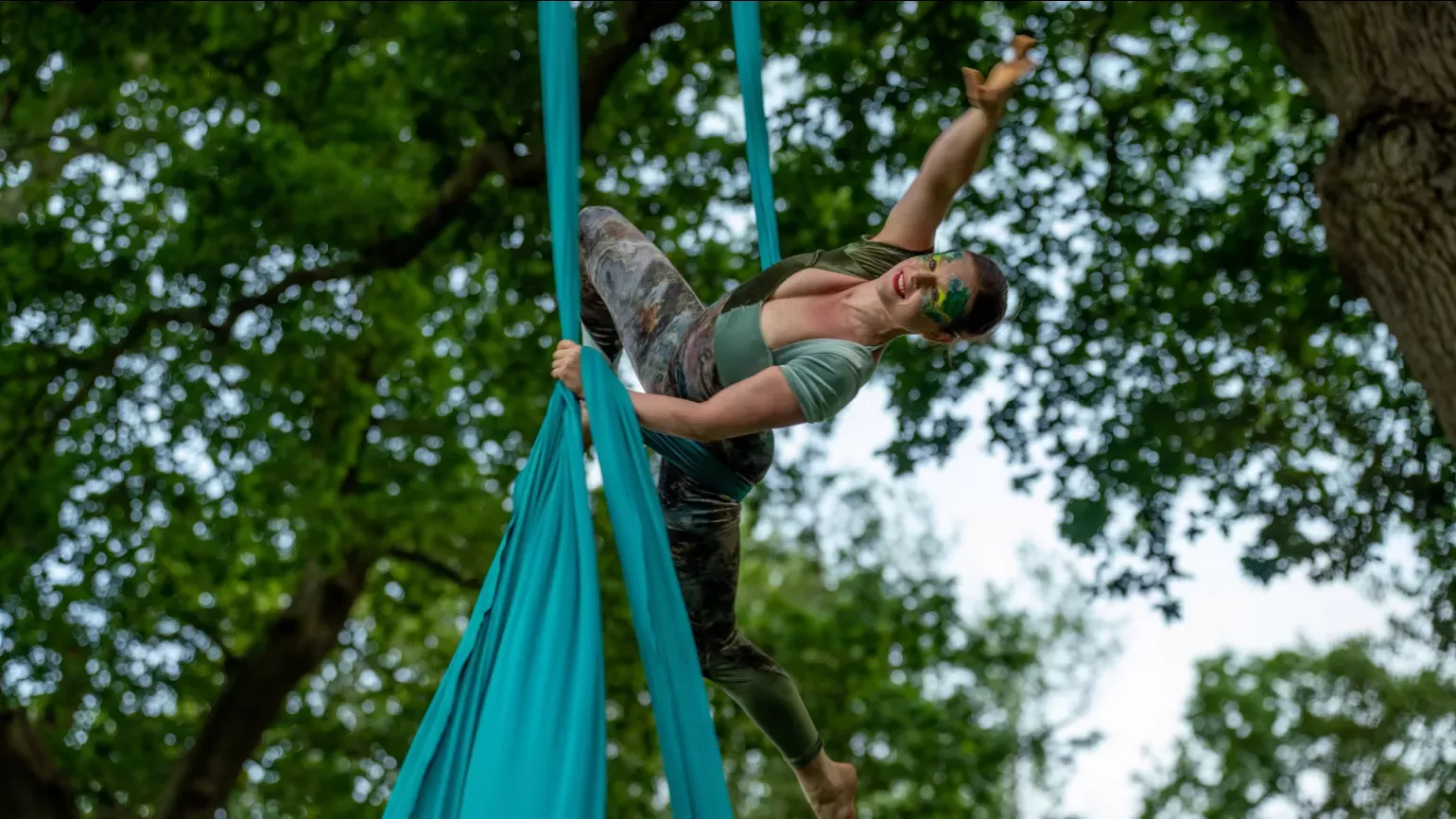 A person on fabric strips dancing from a tree