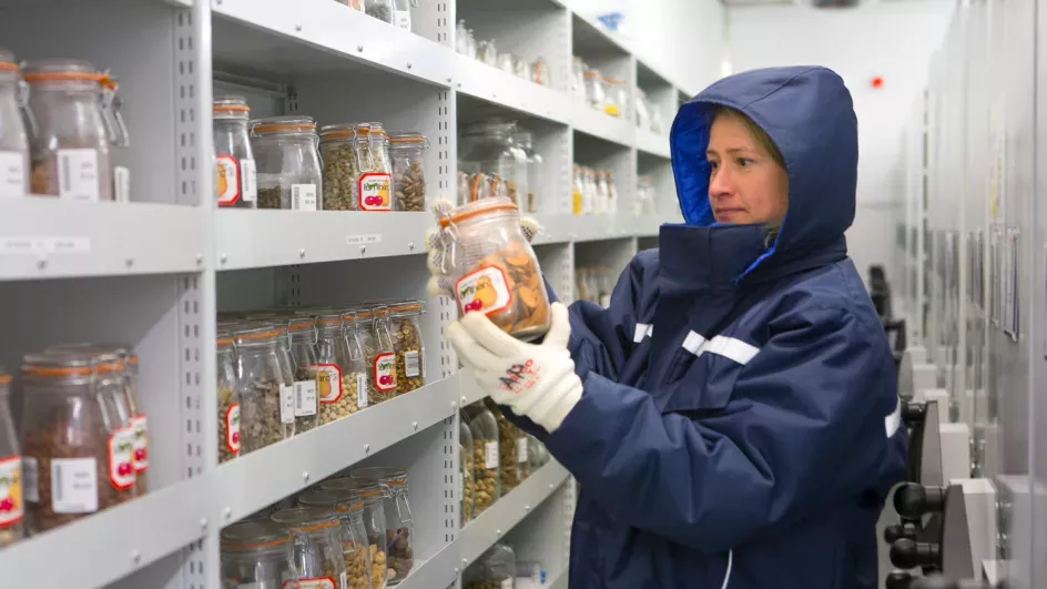 Kew scientist in coat holding jar of seeds