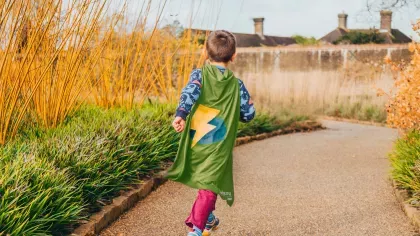 A child runs through a garden at 澳洲幸运8开奖官网开奖 wearing a superhero cap with a lightning bolt on it