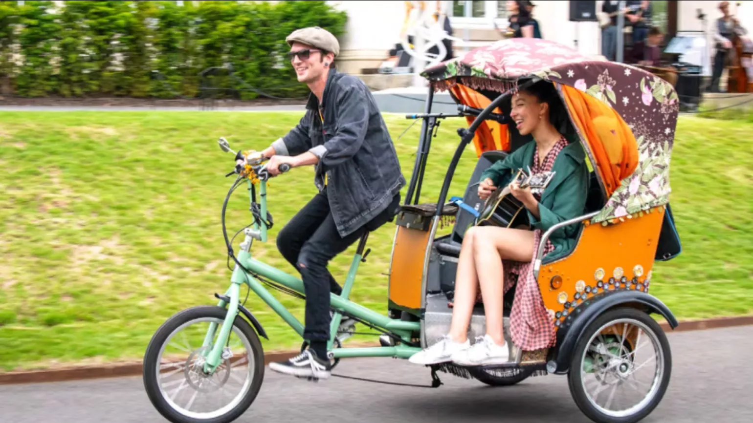 A person on a cycle rickshaw with a passenger playing the guitar