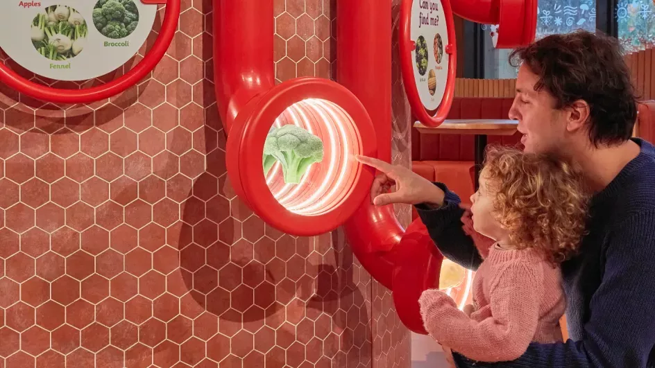 A man and a small child look at a broccoli behind glass