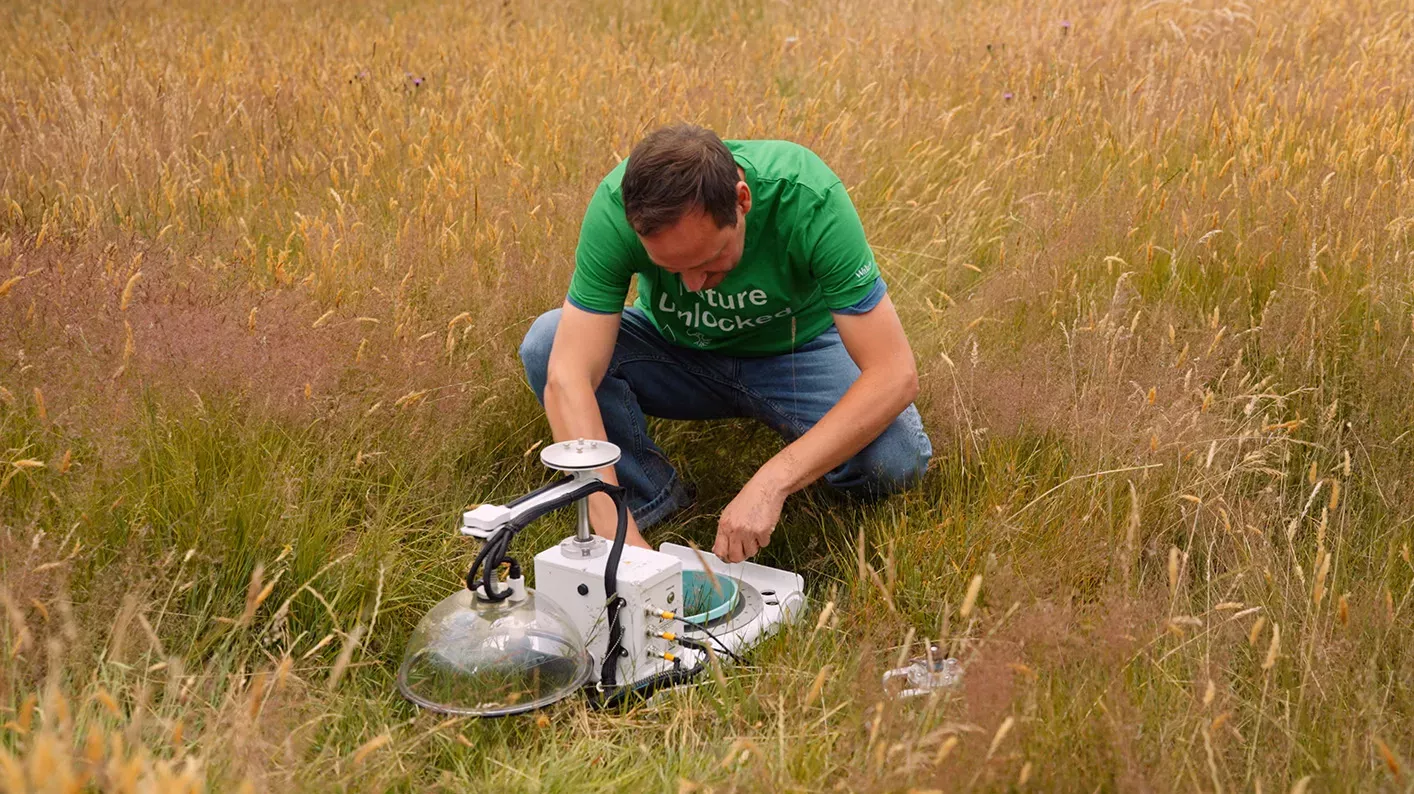 Dr Gary Egan kneels over a gas flux monitoring chamber in a field