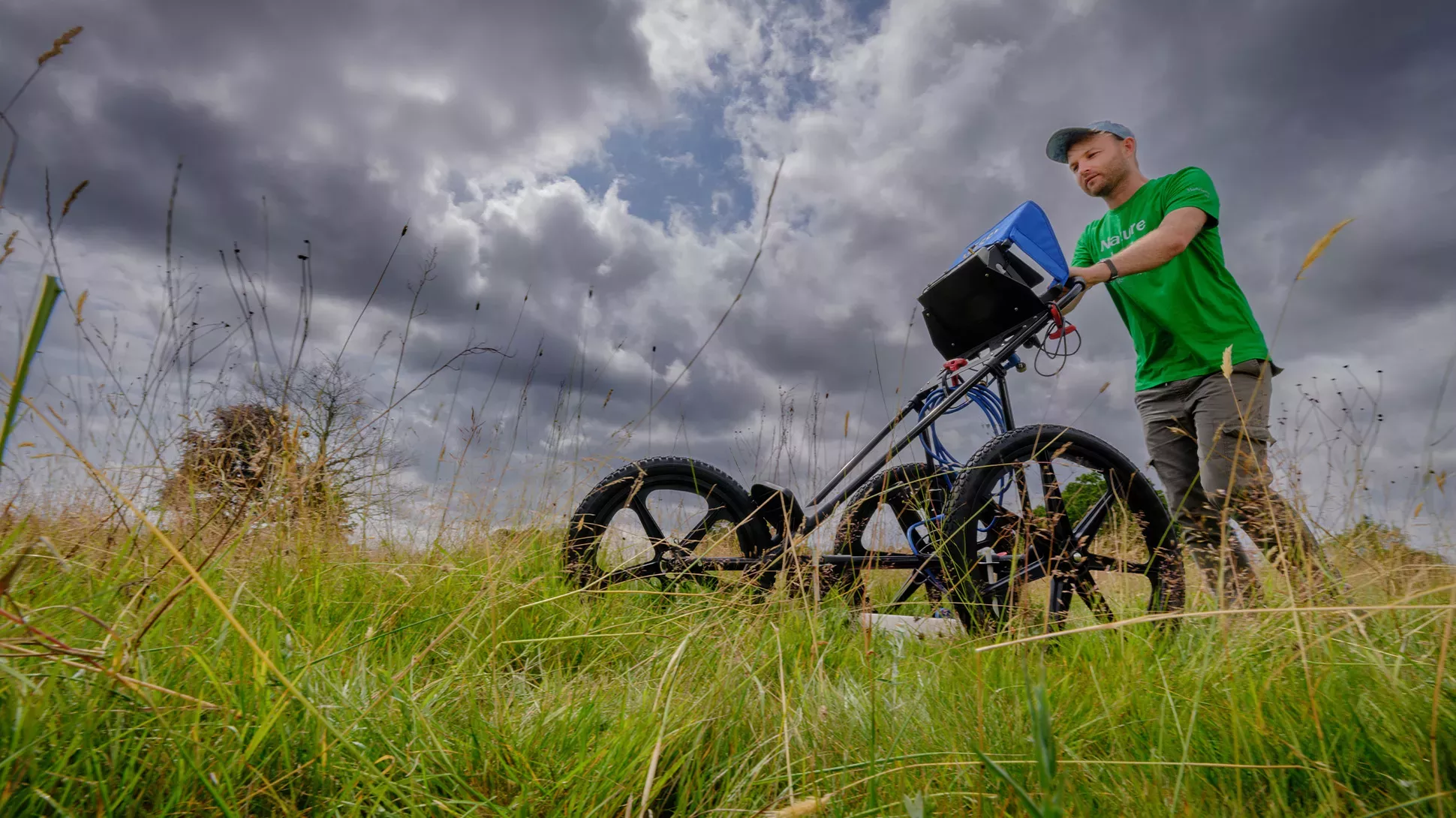 A scientists push a ground-penetrating radar machine through a field.