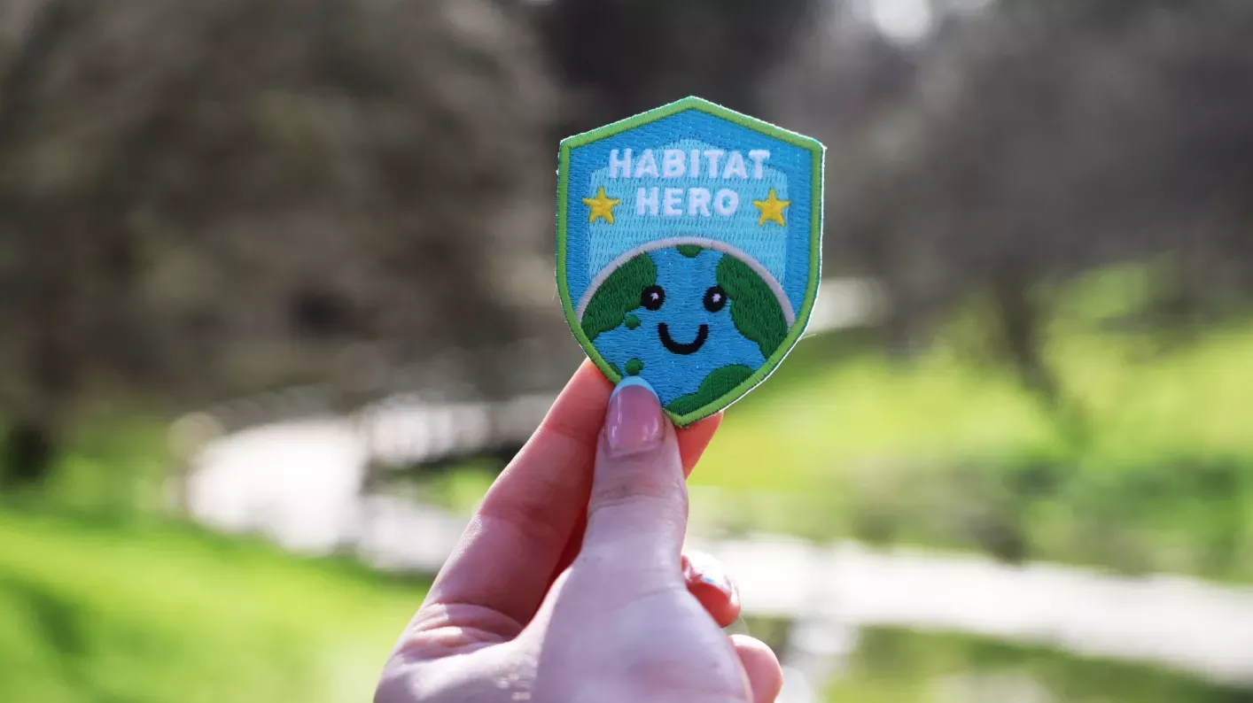 Close up of a blue and green embroidered badge featuring a smiling planet Earth and the words Habitat Hero