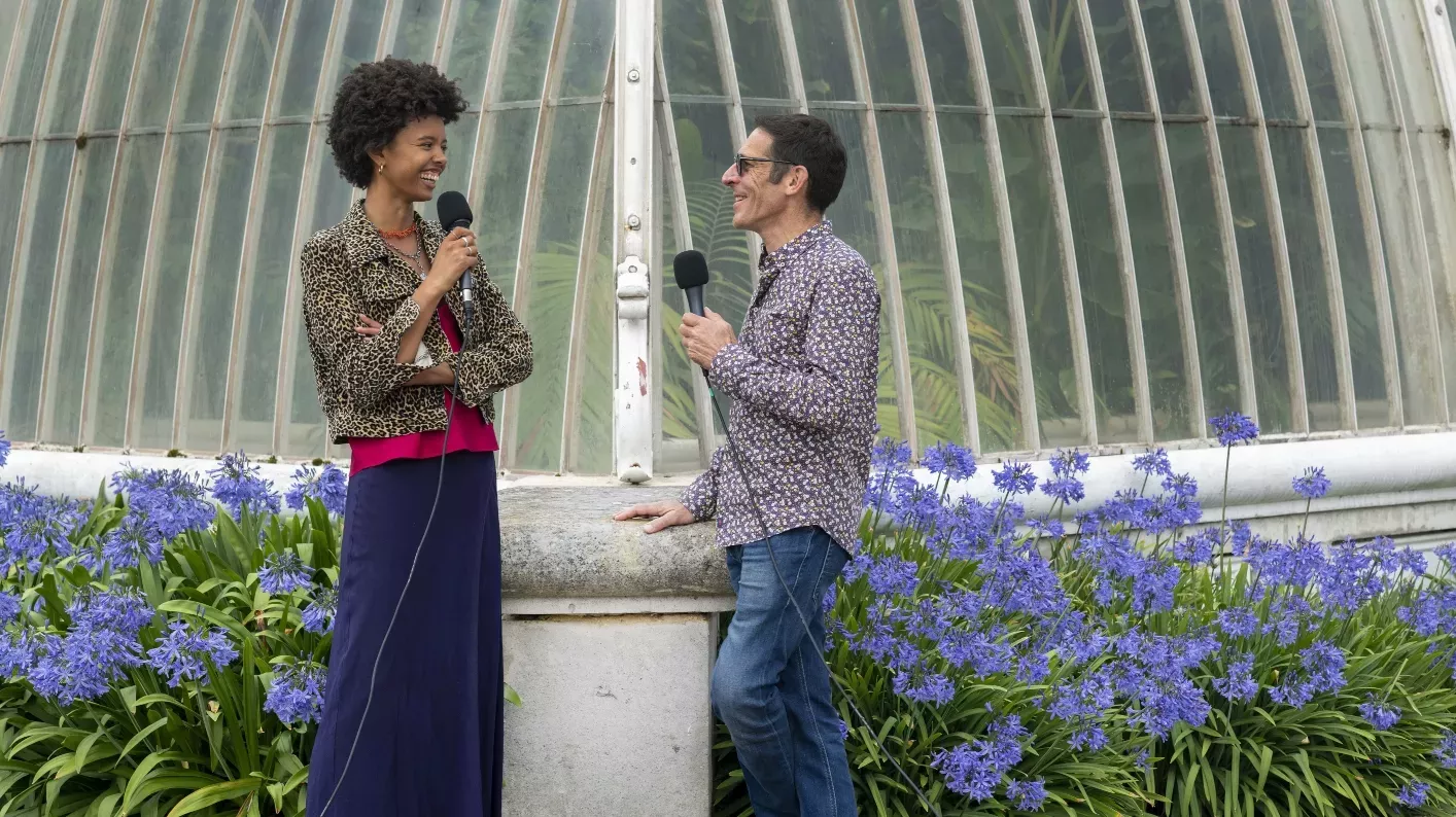 Two people standing outside the Kew's Pal House speaking into microphones