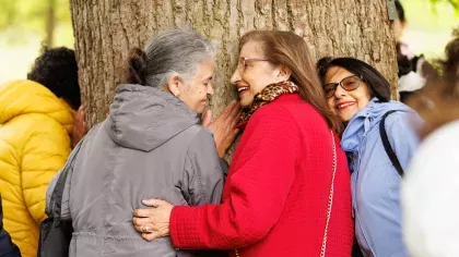 Three women hugging a tree and smiling