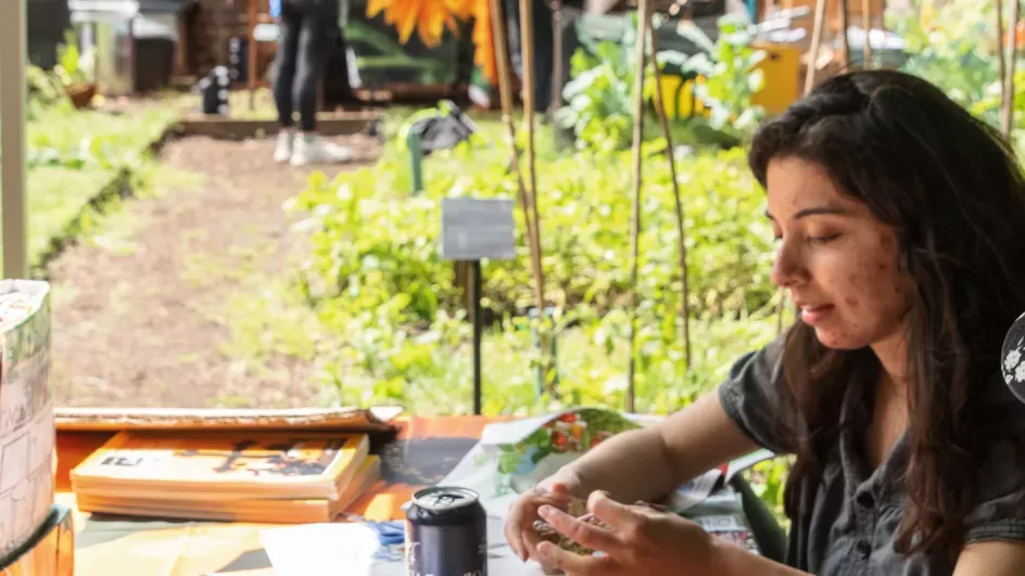 Two people sit at a table covered with craft materials in a garden