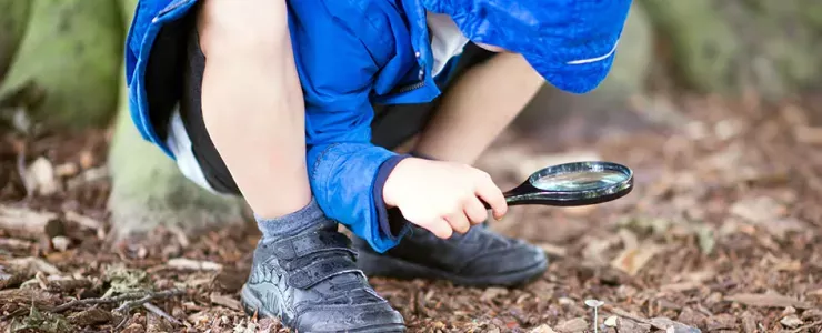 Child looking at the ground using a magnifying glass