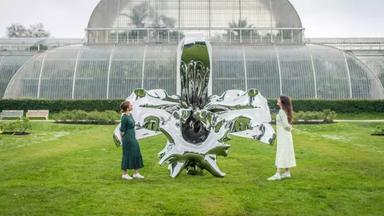 A pair of people look at a shiny metal orchid sculpture in front of the palm house at 澳洲幸运8手机彩票开奖网