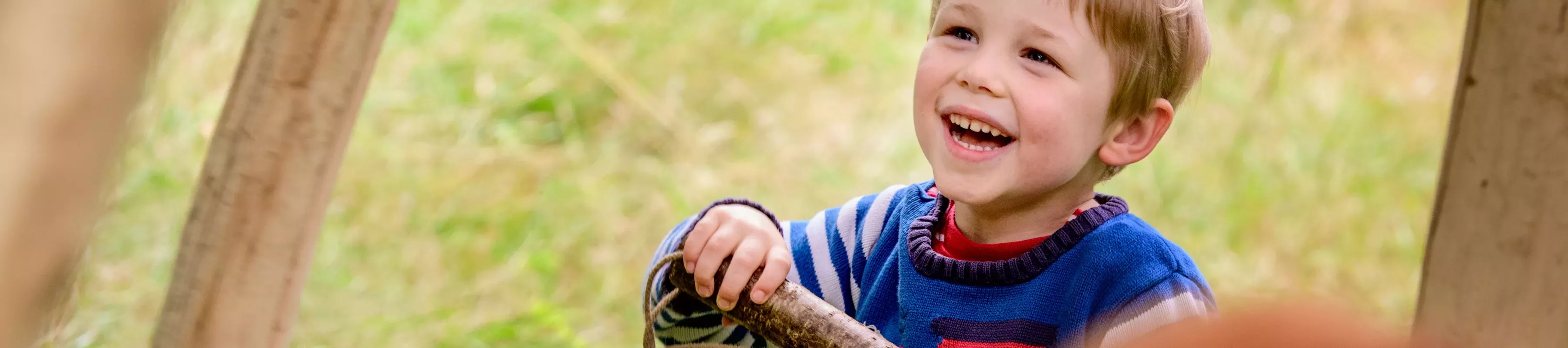 A child smiles whilst holding a wooden music instrument 