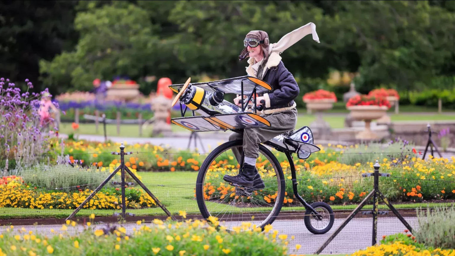 A person dressed as a pilot riding a penny farthing