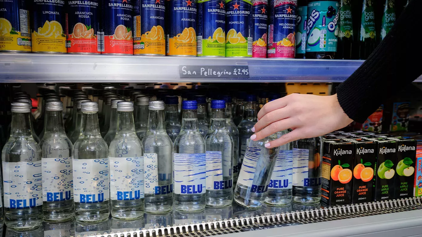 A woman reaches down and grabs a water bottle from a drinks fridge.