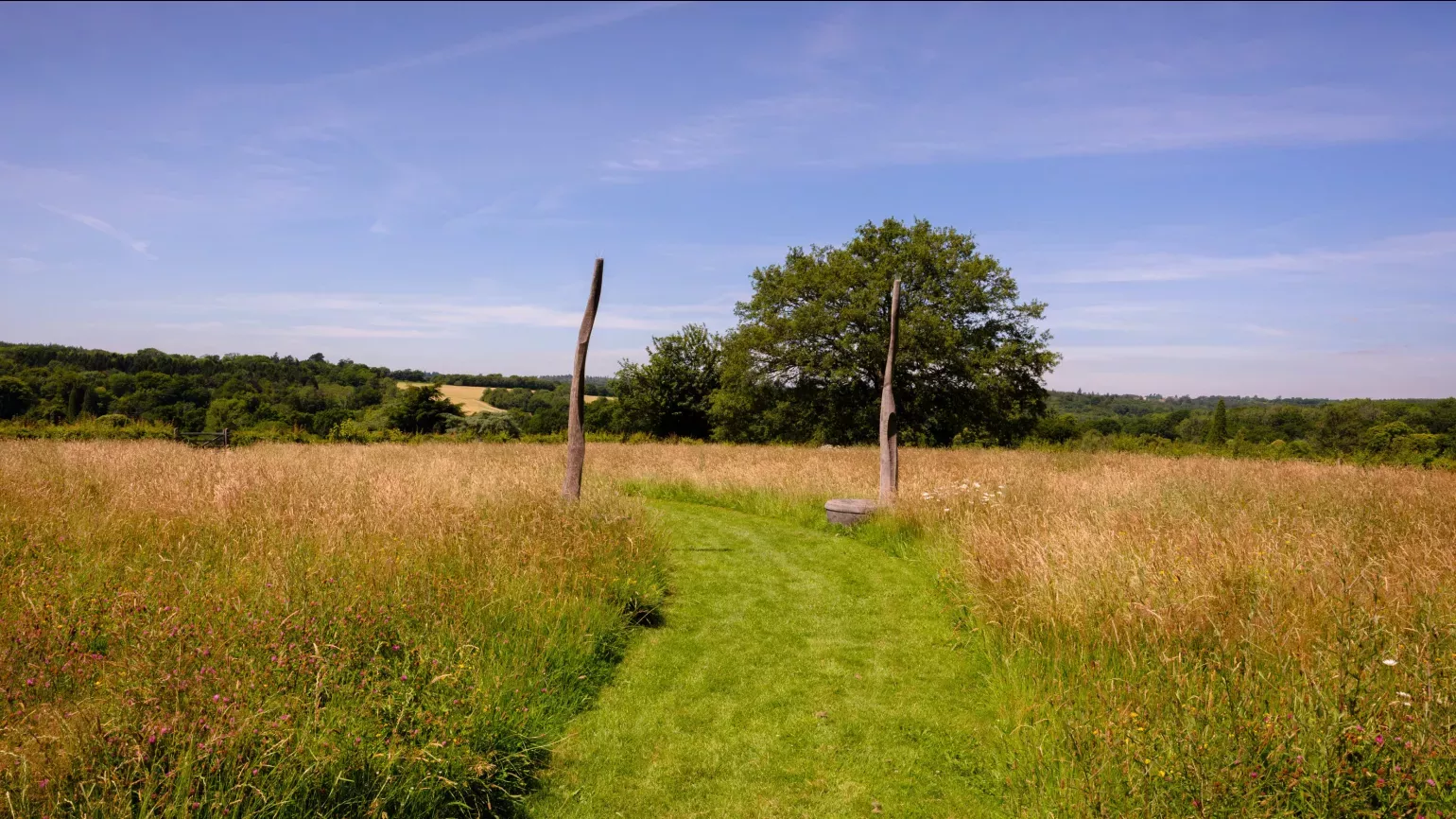 Meadow under blue sky with two tall carved poles on either side of a mown path